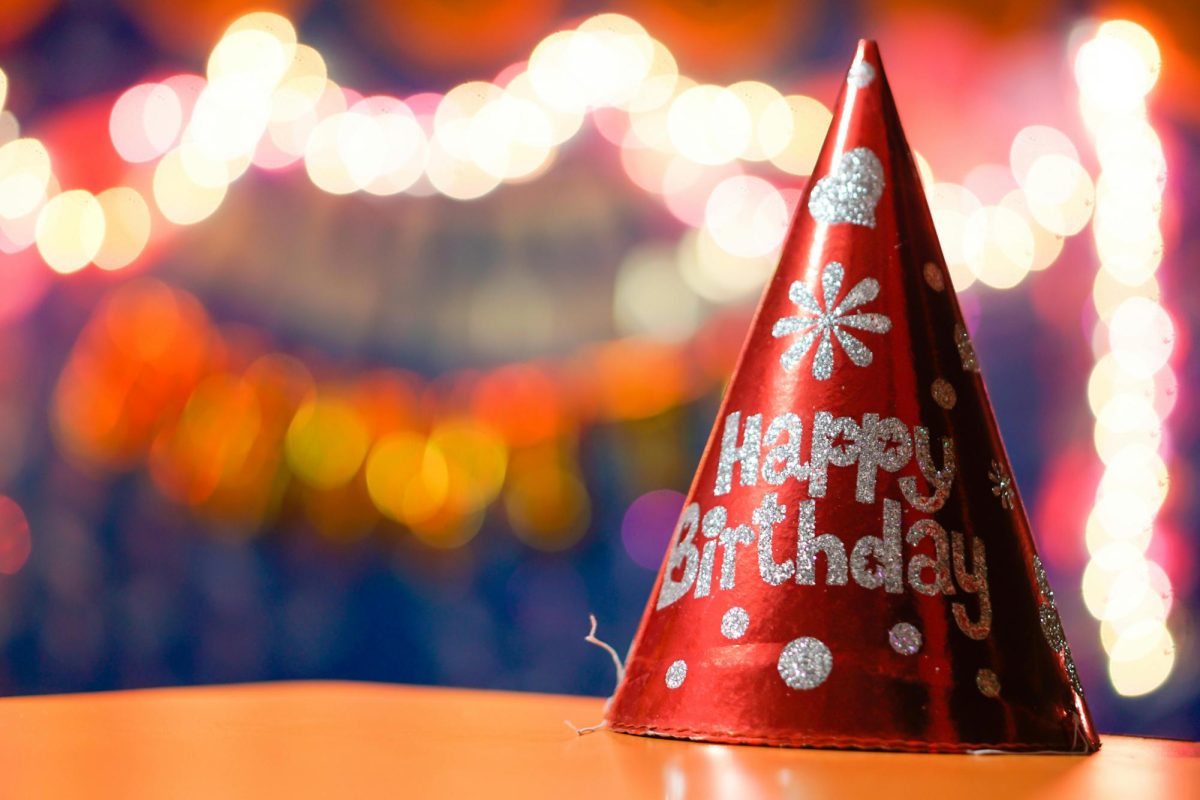 Red party hat that says "Happy Birthday" sitting on a table.